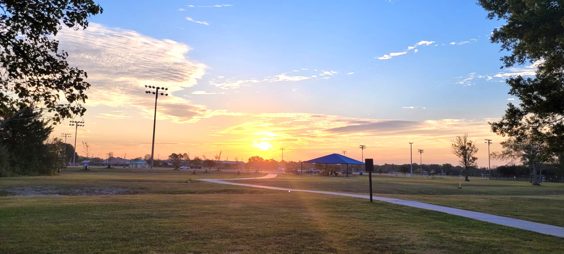 Sunrise over an open park with a walking path and picnic shelter
